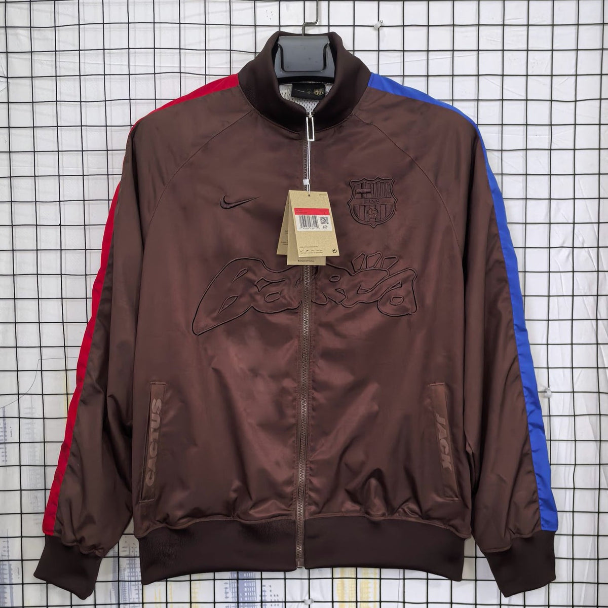 Barca Brown jacket with red and blue accents on a hanger against a grid background