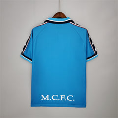 Blue manchester city retro jersey with branding on a gray background